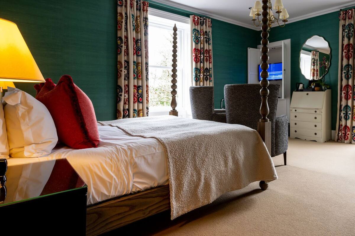 A bedroom with a four-poster bed, a bedside lamp, a chair, a dresser, and a mirror.