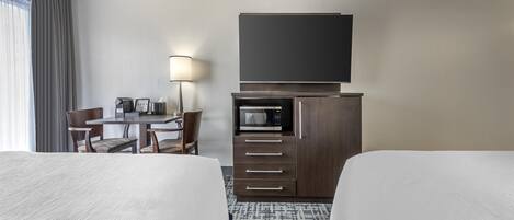 Una habitación de hotel con dos camas, un escritorio con lámpara, microondas y televisor en un mueble.