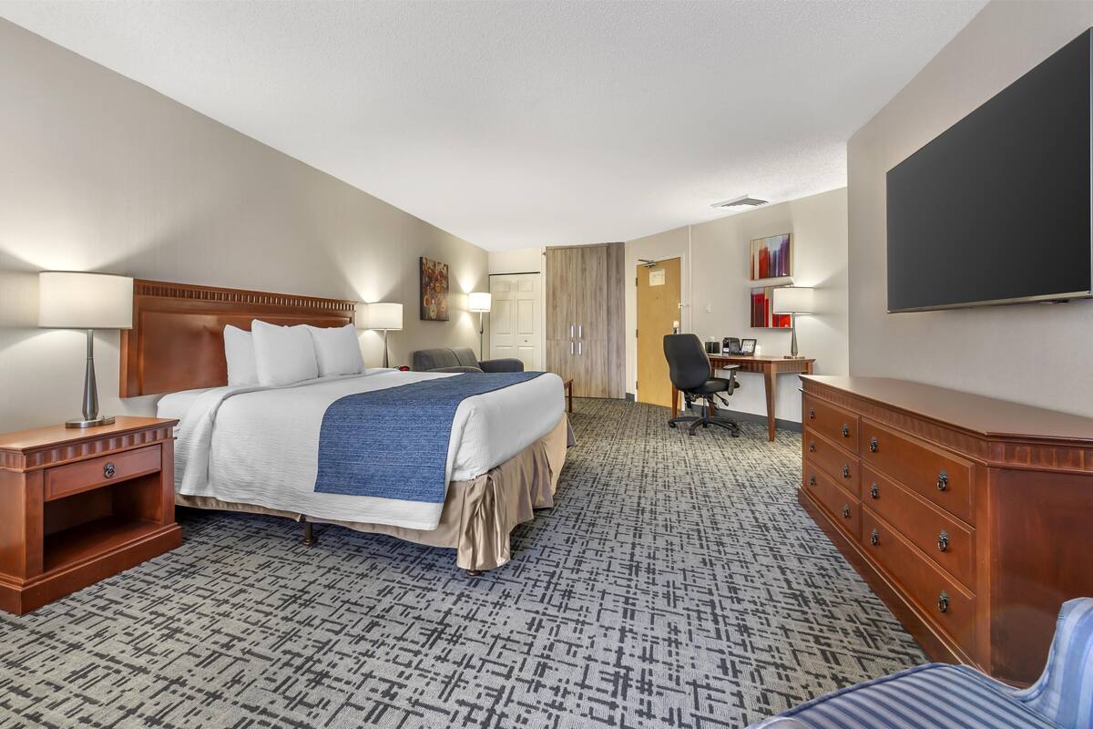 A hotel room with a bed, desk, chair, dresser, and a TV.