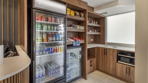 A kitchenette with a refrigerator stocked with beverages, a microwave, and shelves with snacks. - Best Western Hotel Brossard (Brossard)