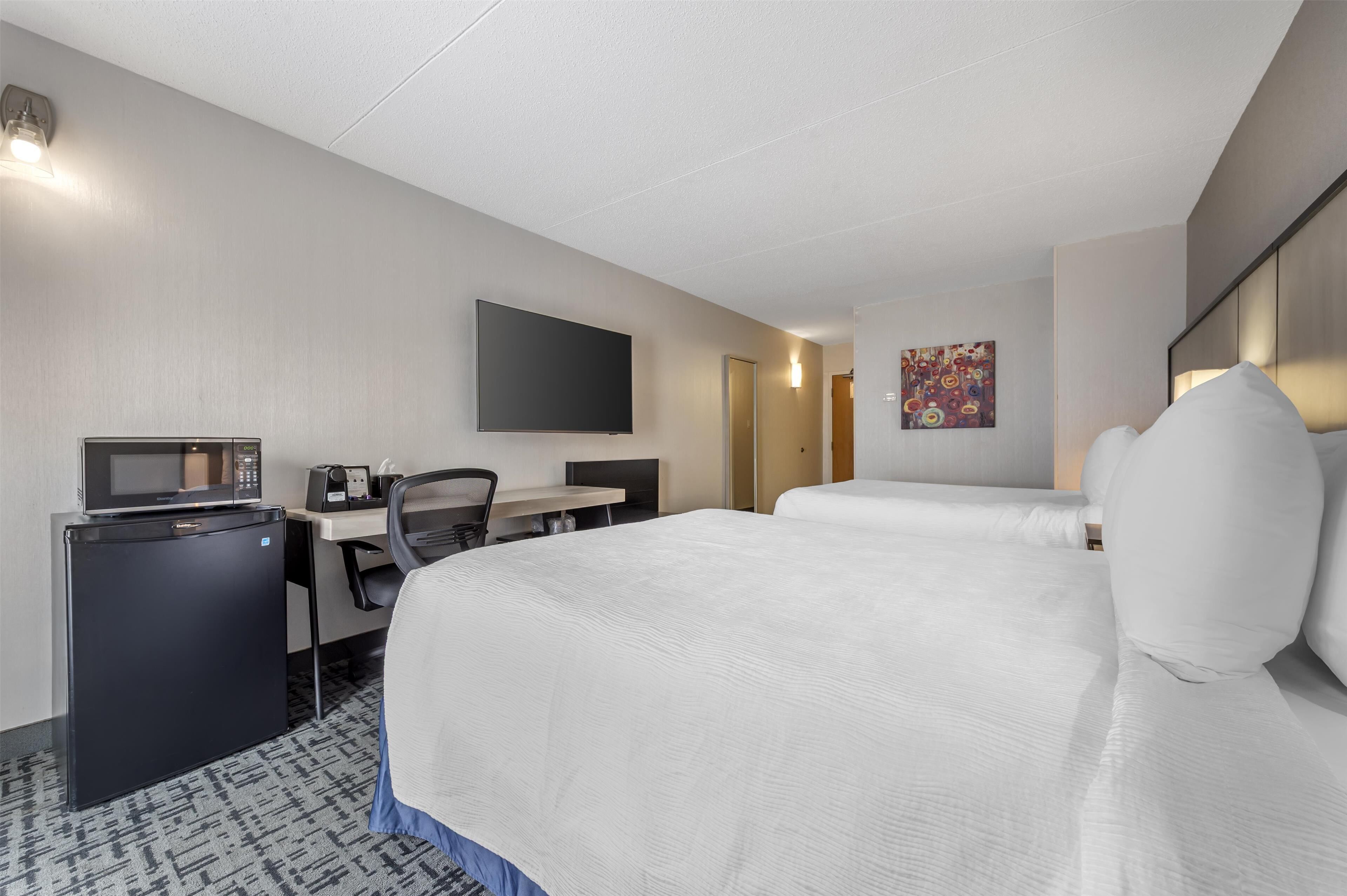 A hotel room with a bed, desk, chair, and a flat-screen TV.
