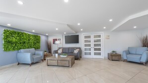 A modern living room with a green wall, two sofas, a coffee table, and a TV mounted on the wall. - Best Western Hotel Brossard (Brossard)