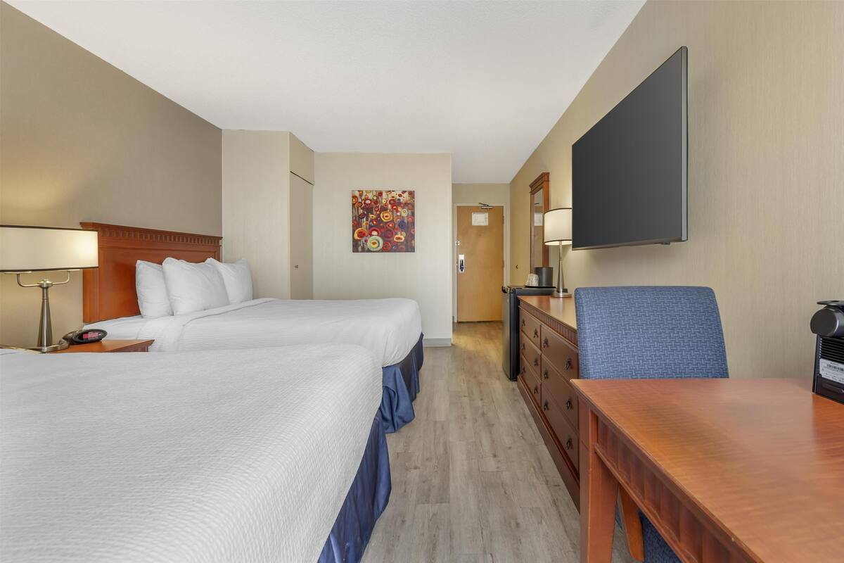 A hotel room with two beds, a desk, a dresser, a flat-screen TV, and a painting on the wall.