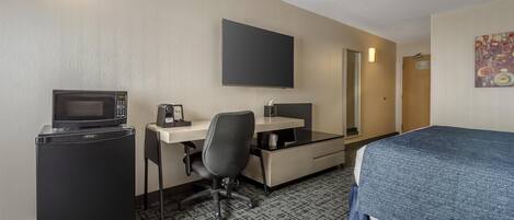 A hotel room with a bed, a desk with a computer, a microwave, and a refrigerator.