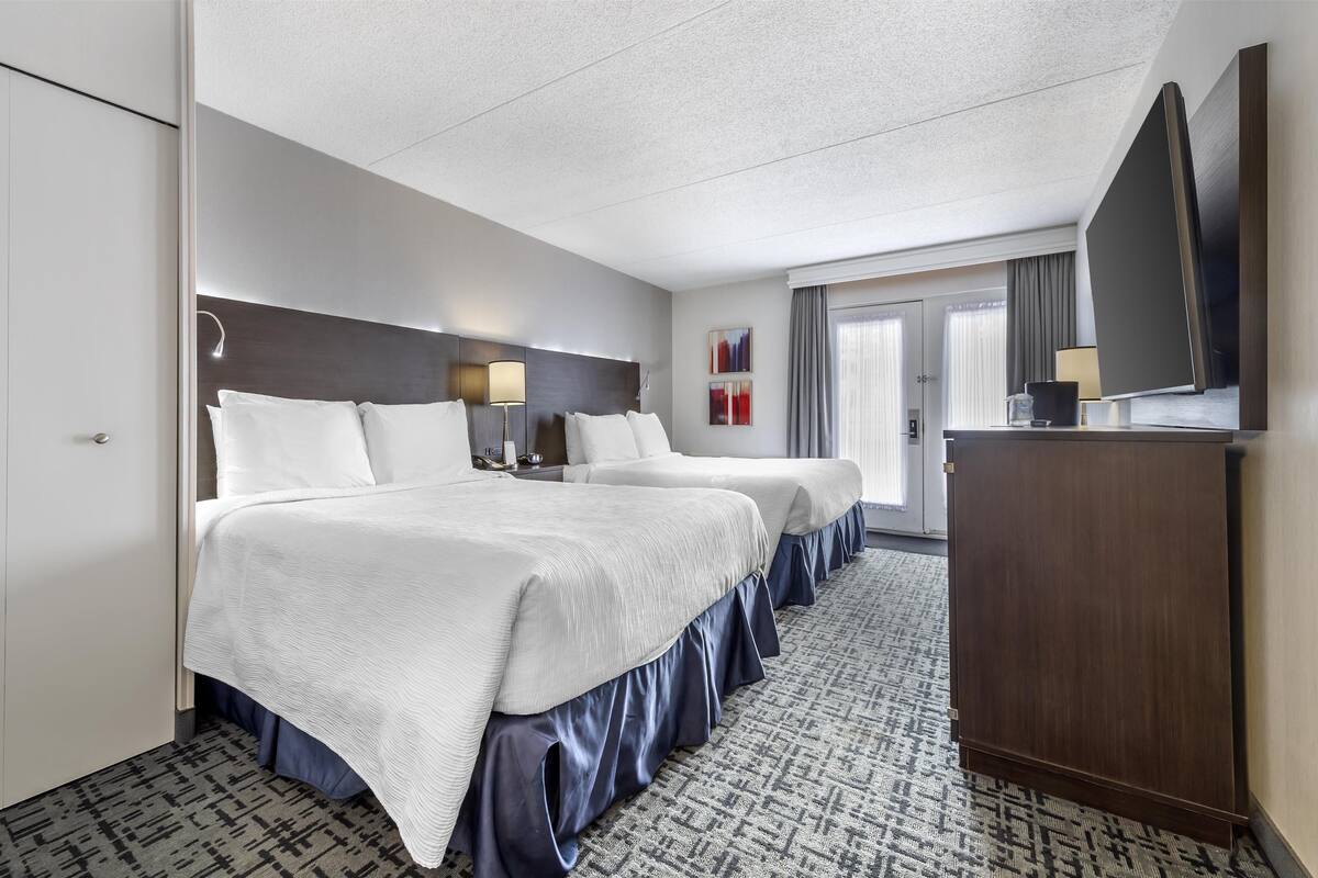 A hotel room with two beds, a desk, a flat-screen TV, and a patterned carpet.