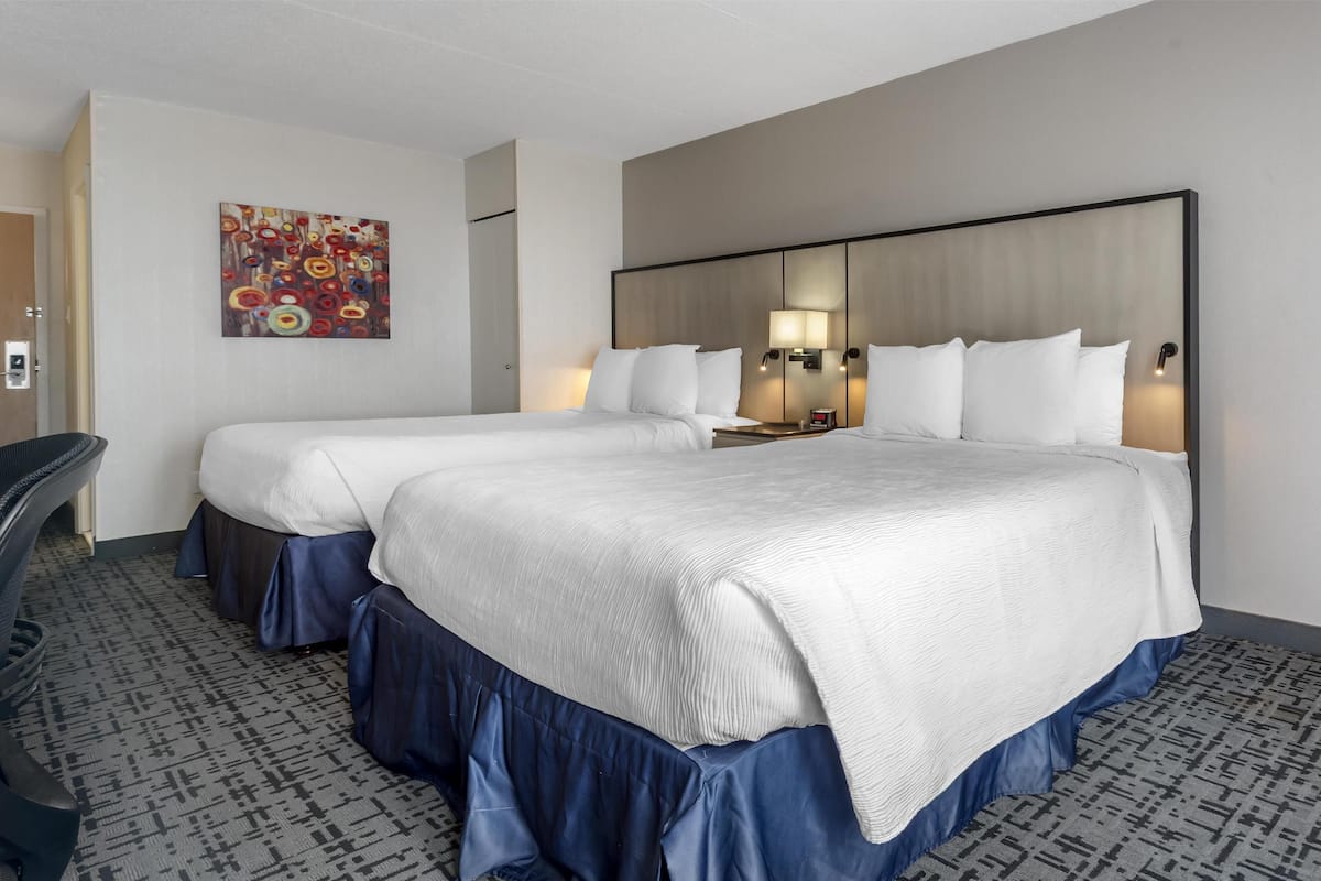 A hotel room with two beds, a desk, and a chair.