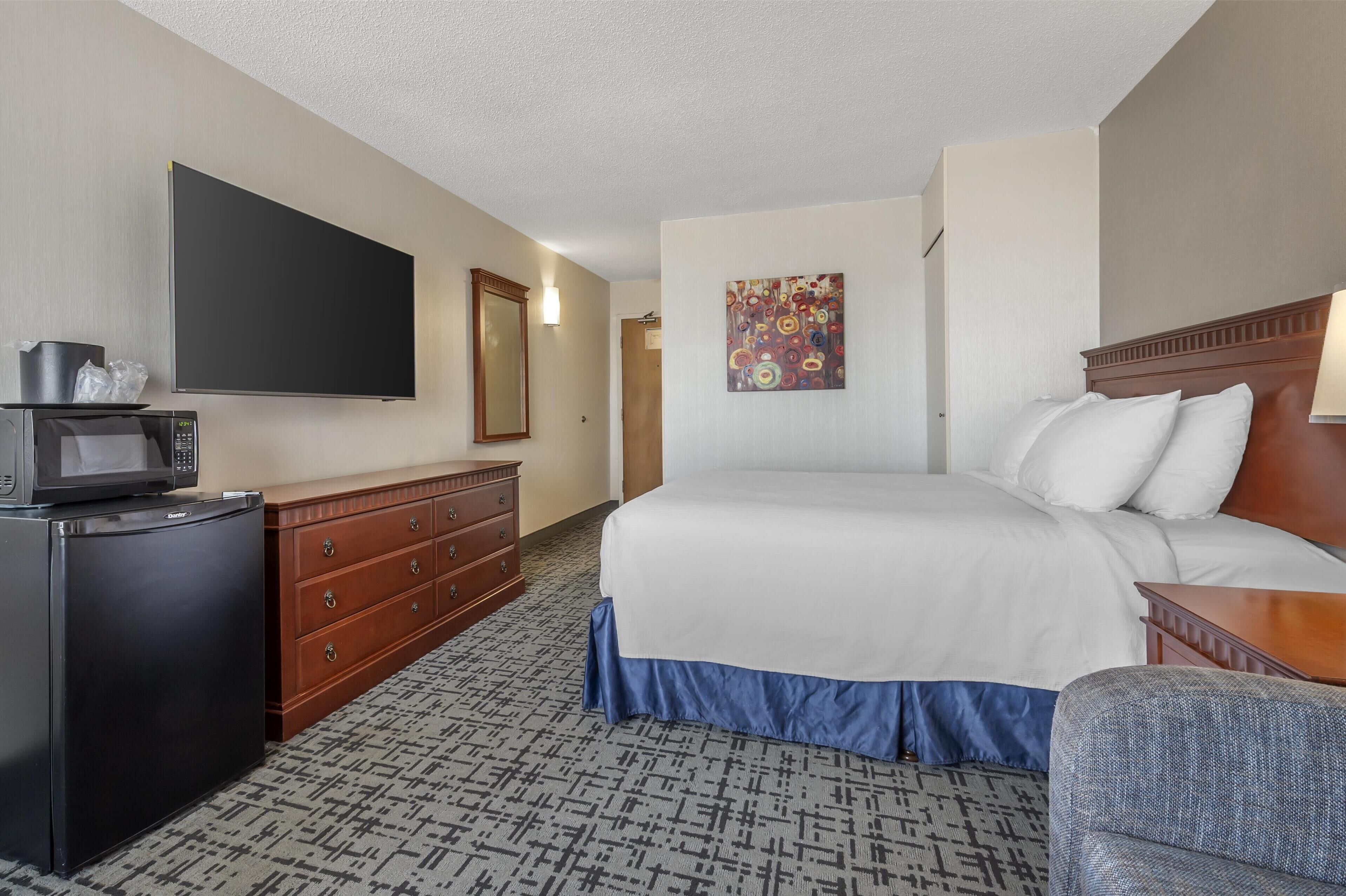 A hotel room with a bed, a dresser, a microwave, a flat-screen TV, and a painting on the wall.