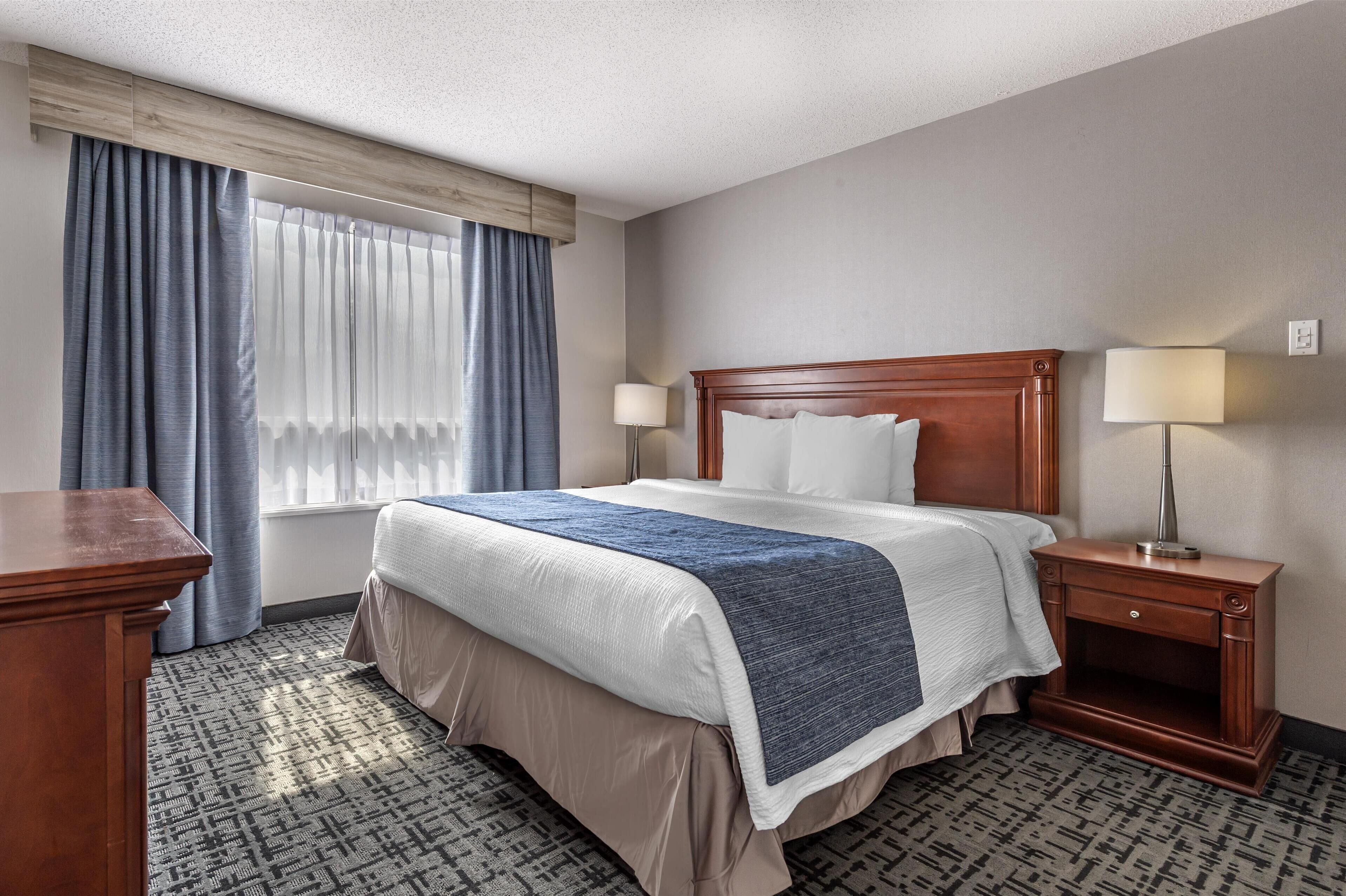 Ein Hotelzimmer mit einem Bett, Nachttischen, einem Schreibtisch und einem Vorhangfenster.