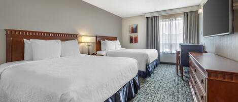 A hotel room with two beds, a dresser, a desk, and a flat-screen TV.