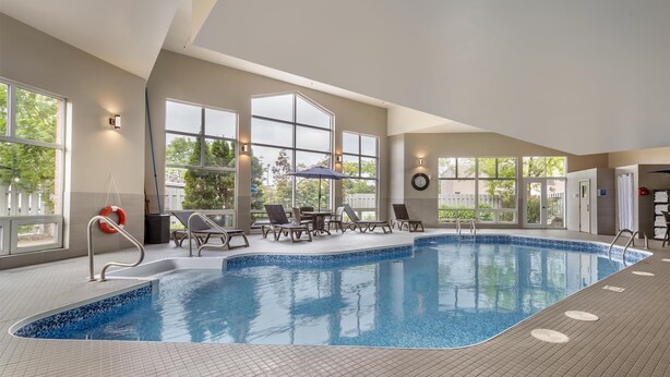An indoor swimming pool with clear glass walls, lounge chairs, and a lifebuoy. - Best Western Hotel Brossard (Brossard)