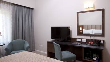 Quarto de hotel com cama, escrivaninha com televisão, cadeira, cômoda e espelho.