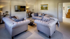 A living room with two tufted sofas, a coffee table, a flat-screen TV, and a painting on the wall. - Sudbury House Hotel (Faringdon)
