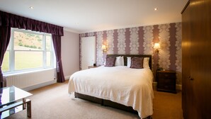 A bedroom with a large bed, two bedside lamps, a window with curtains, a radiator, and a wooden wardrobe. - The Izaak Walton Hotel (Ashbourne)