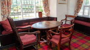 A room with a round wooden table and four chairs, a bench along the window, and a plaid carpet. - The Izaak Walton Hotel (Ashbourne)