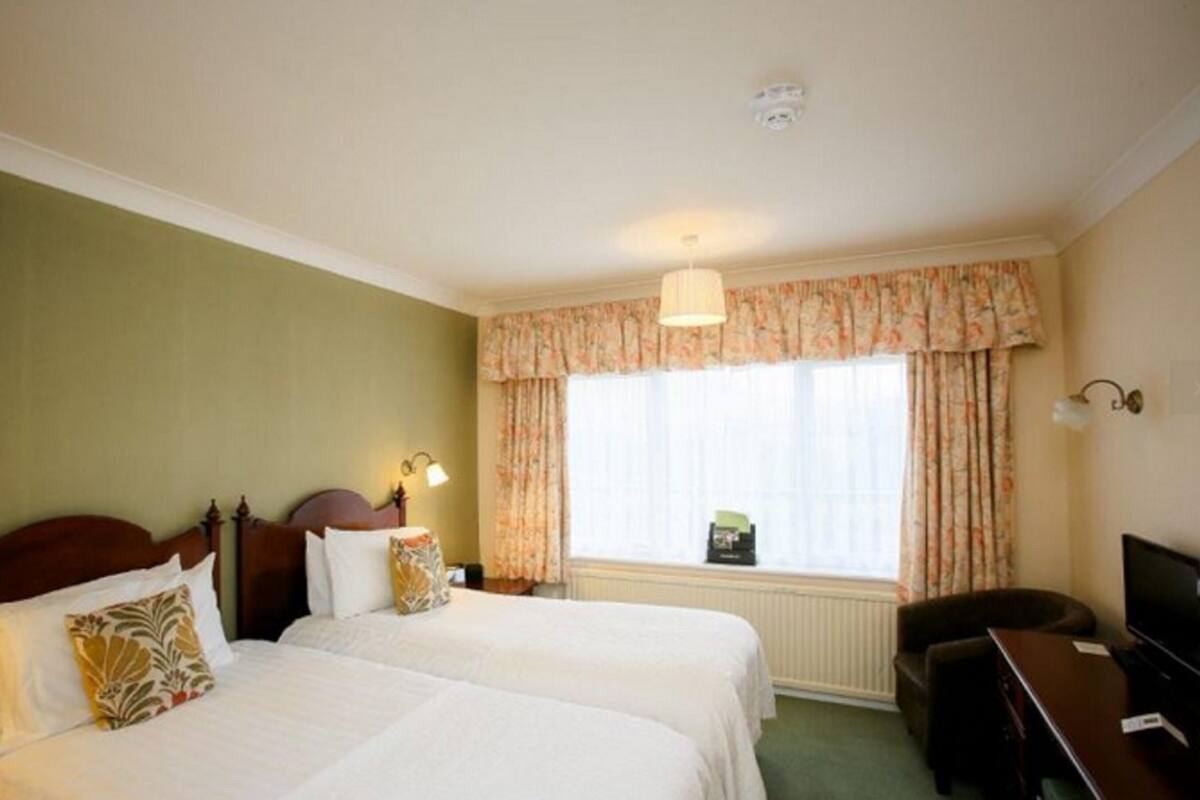 Habitación de hotel con dos camas, un escritorio, un televisor y una ventana con cortinas.