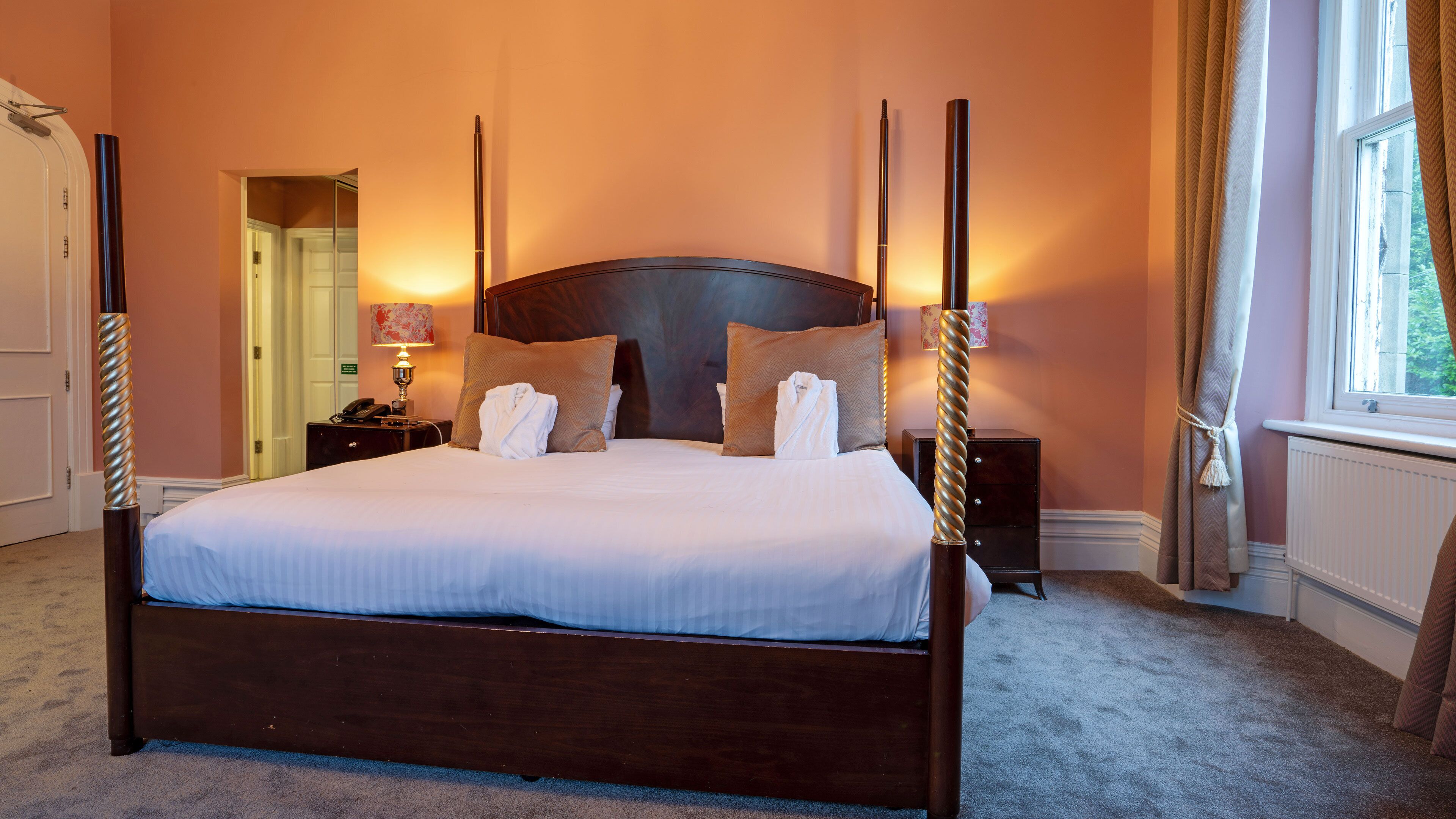 A large bed with a wooden headboard, a bedside table with a lamp, and a nightstand with a phone.