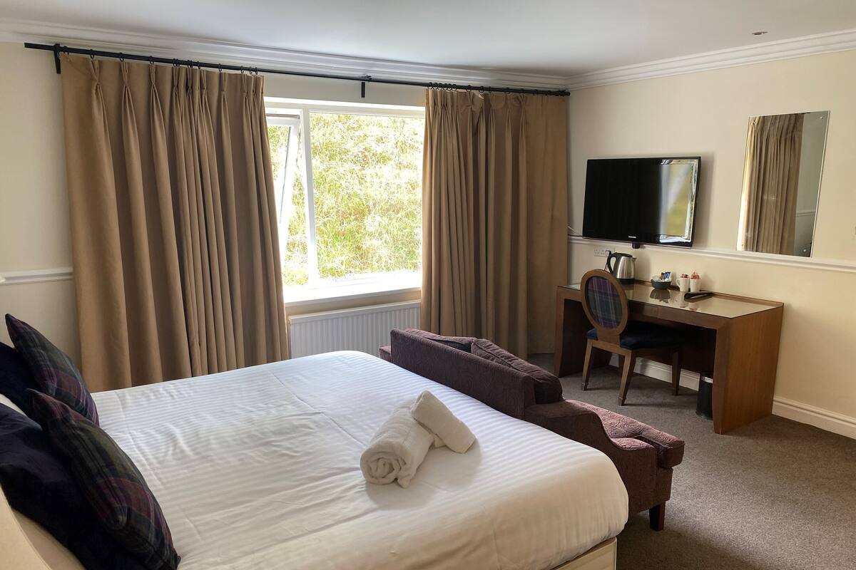 A hotel room with a large bed, a desk, a chair, a television, and a window with curtains.