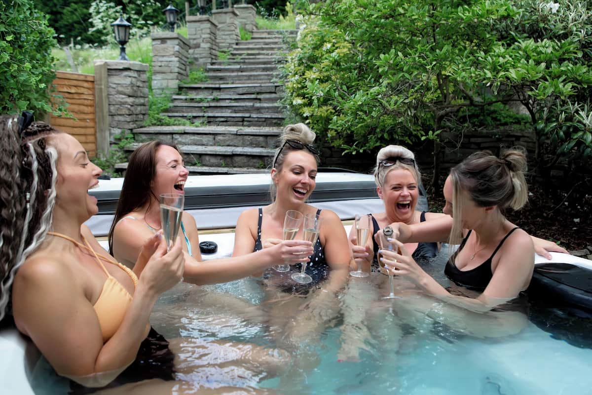 A group of people in a hot tub with a stone staircase and greenery in the background.