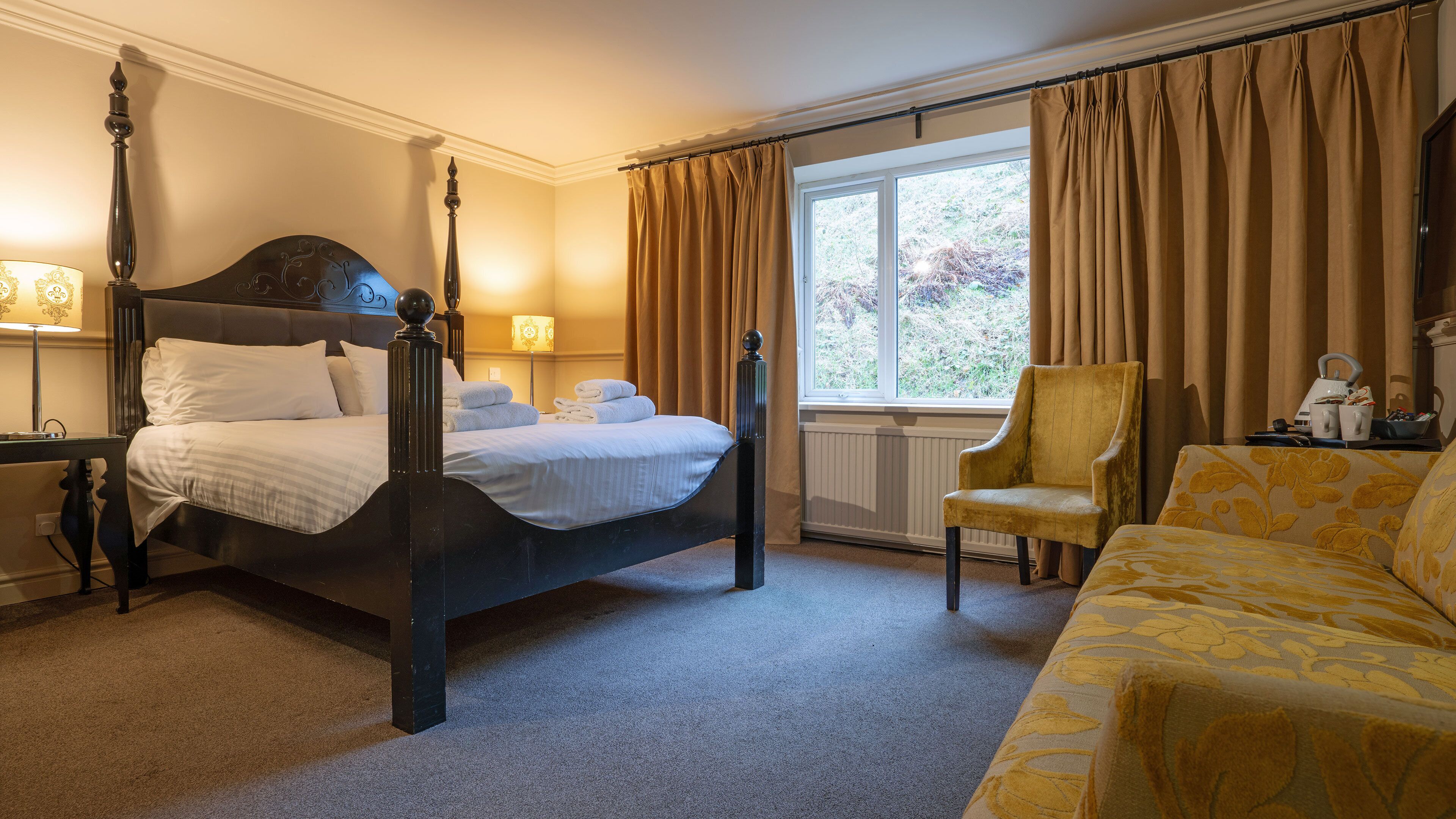 A four-poster bed with a headboard, a sofa, a chair, and a window with curtains.