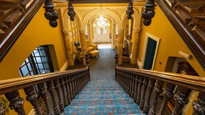 A grand staircase with ornate railings and a patterned carpet leading to a room with a chandelier. - Hollin House Hotel (Macclesfield)