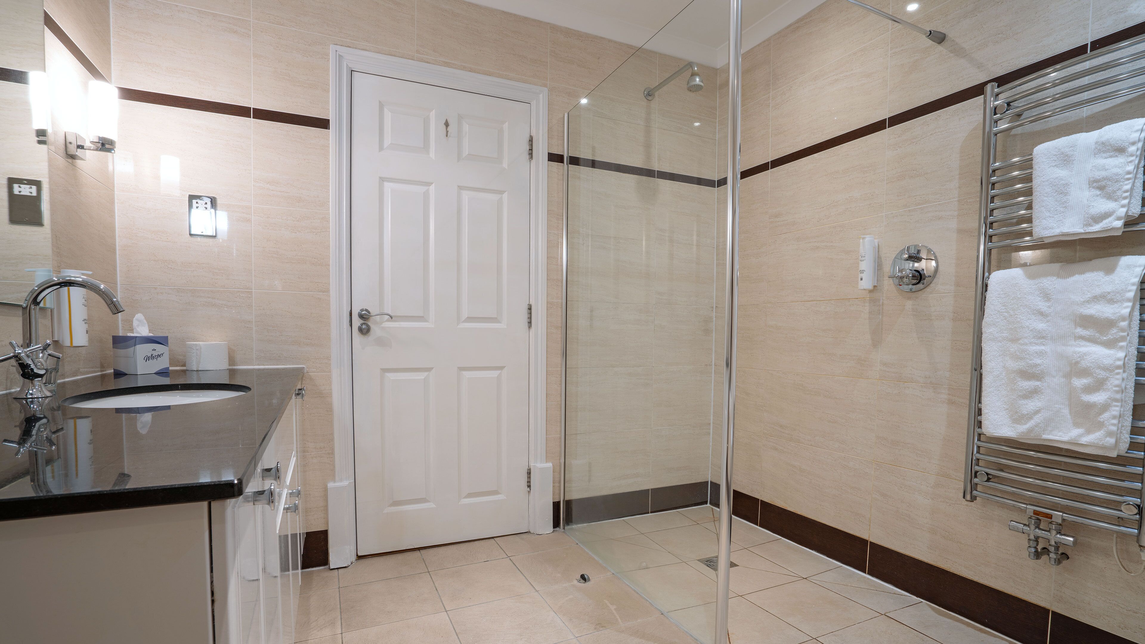 Un baño moderno con ducha de vidrio, lavamanos con espejo y toallero con toallas.