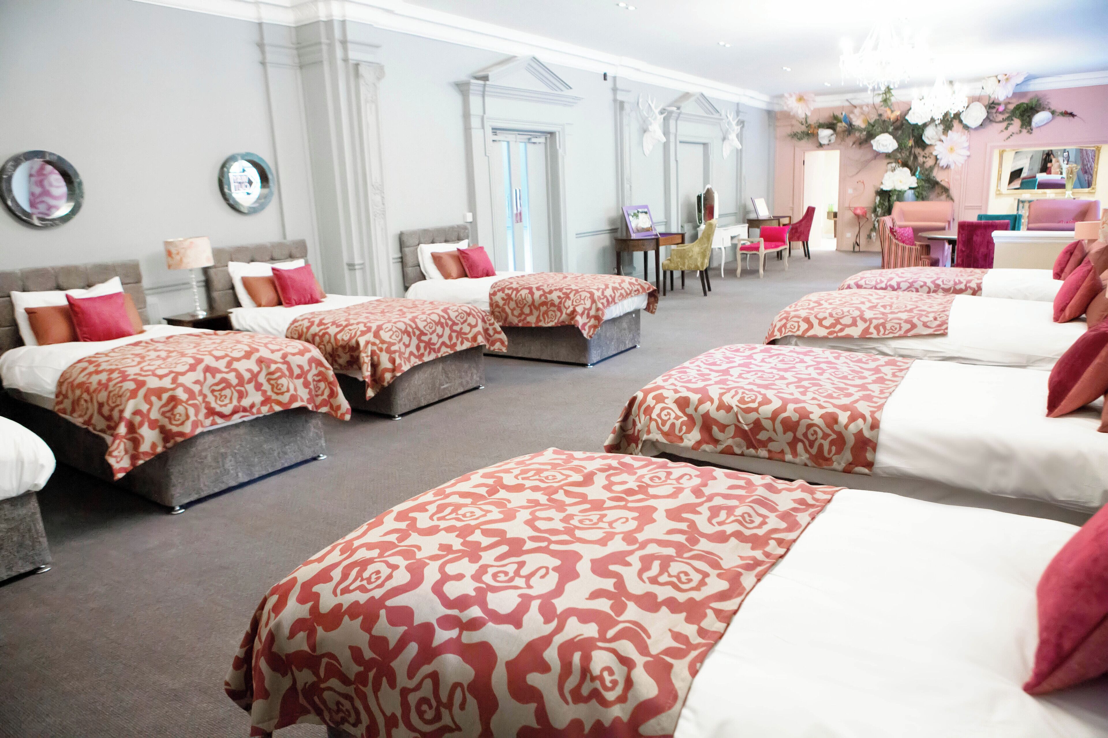 Habitación de hotel con varias camas, cada una con una colcha estampada, un escritorio con silla, y una pequeña mesa con una silla.