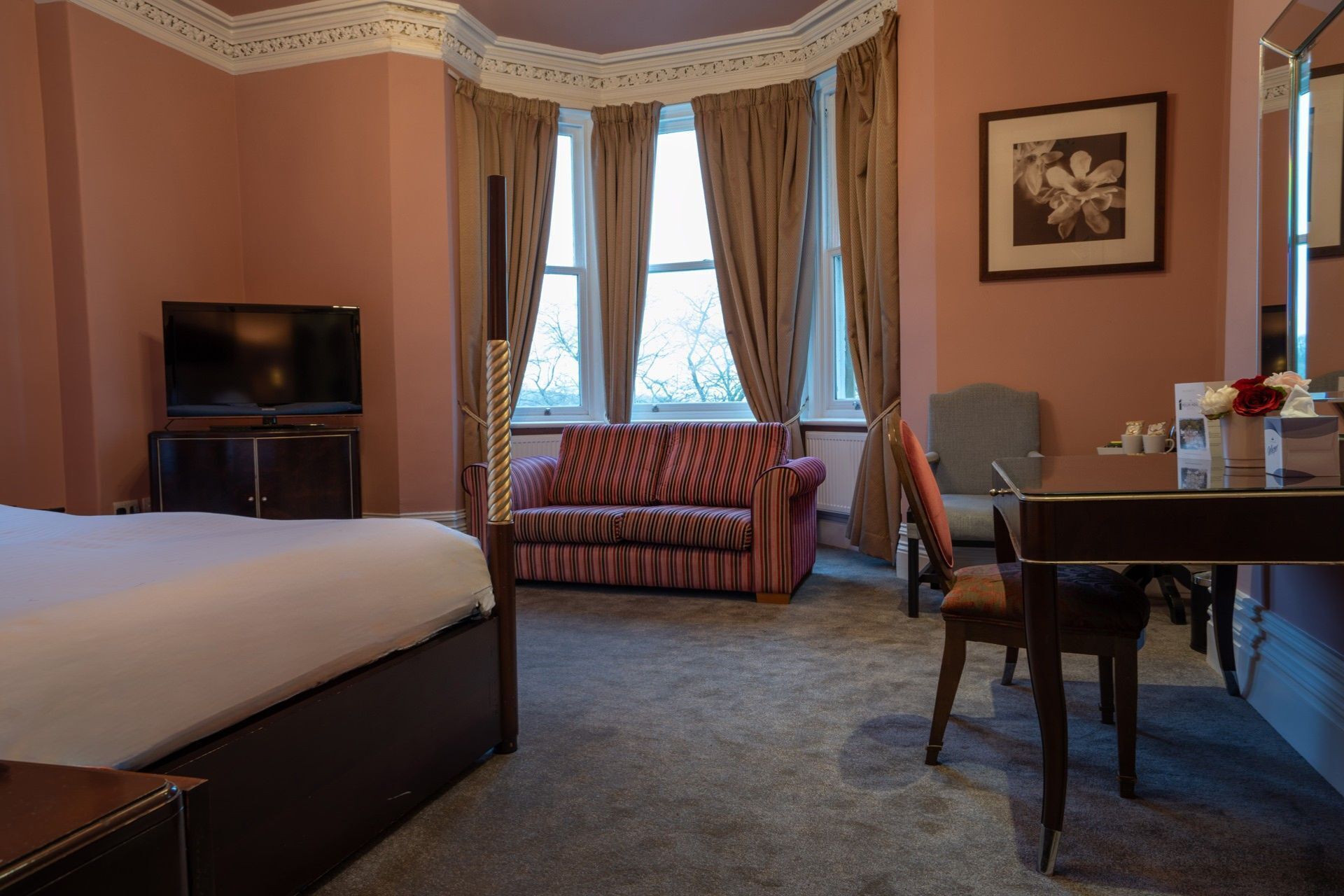 A hotel room with a bed, a sofa, a TV, a dining table, and a chair.
