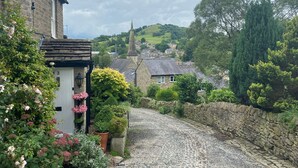 A cobblestone street in a village with stone buildings, a church spire, and lush greenery. - Hollin House Hotel (Macclesfield)