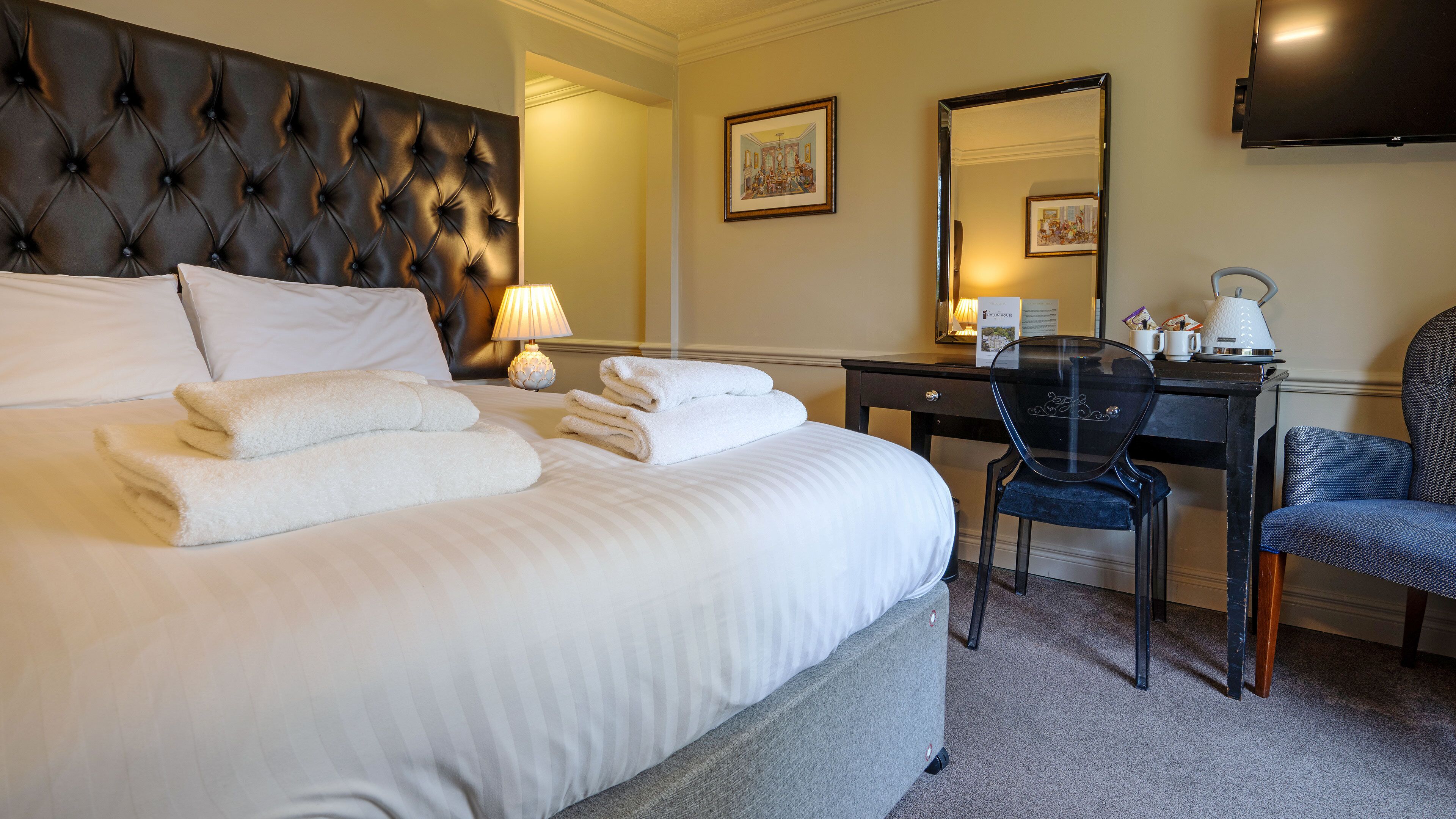 Habitación de hotel con una cama grande, un escritorio, una silla y un televisor en la pared.