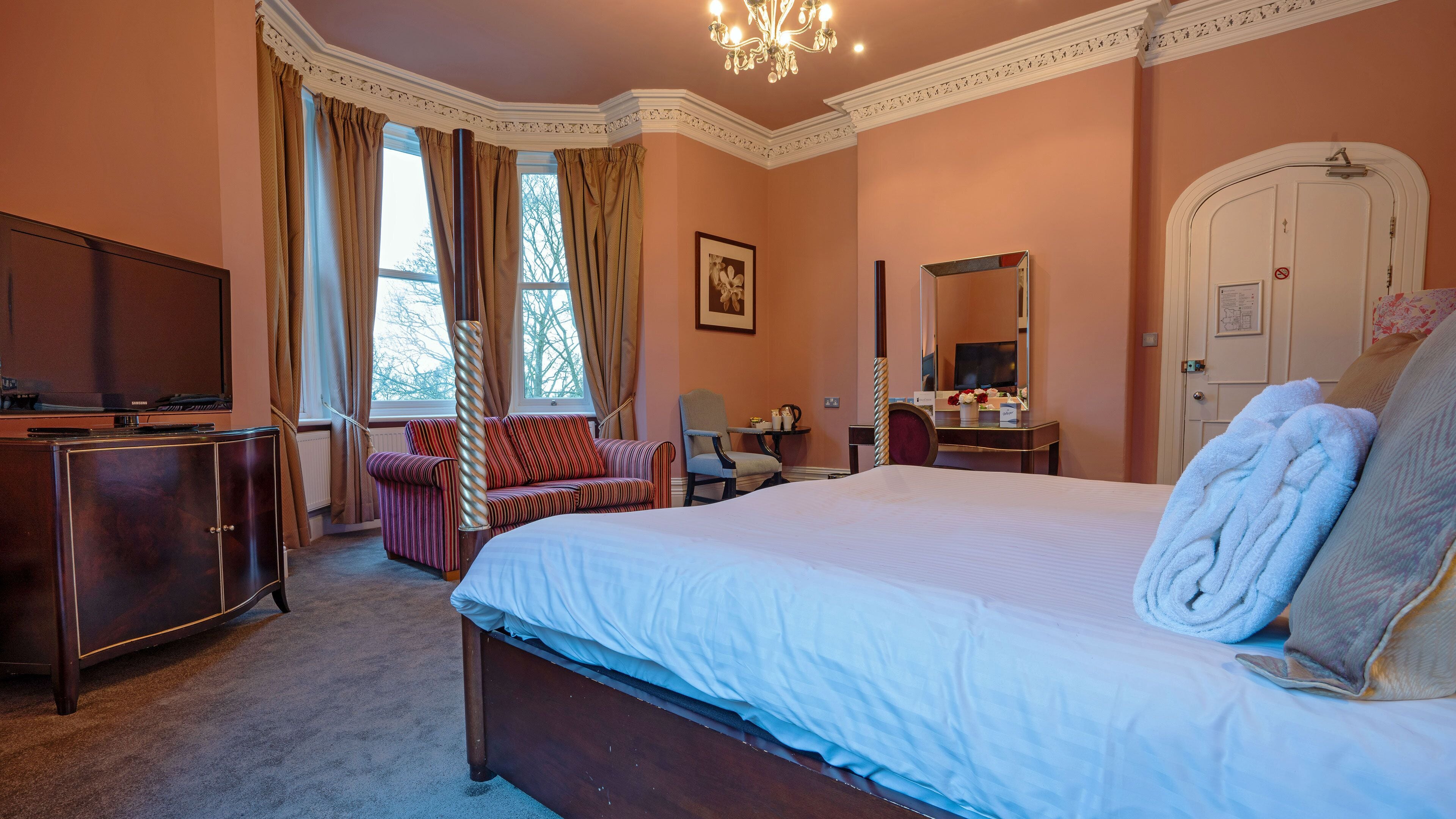 A hotel room with a large bed, a television, a desk with a chair, and a window with curtains.