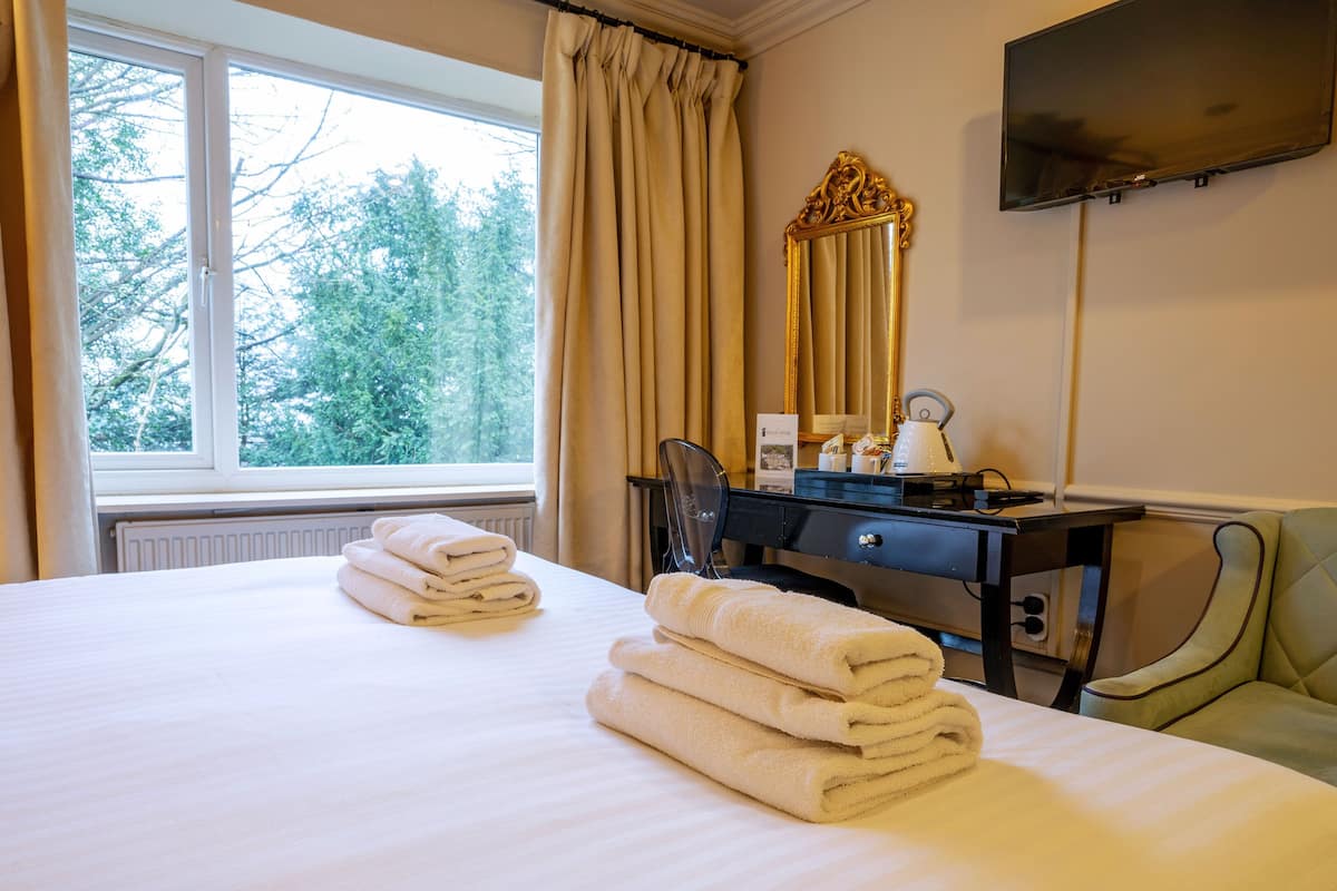 A hotel room with a bed, a desk with a chair, a television, and a window with curtains.