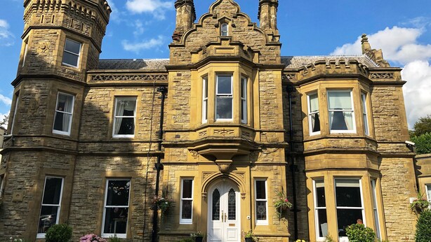 A historic stone building with a prominent turret and bay windows, featuring a central entrance with a white door. - Hollin House Hotel (Macclesfield)