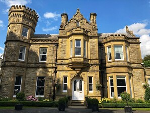 A historic stone building with a prominent turret and bay windows, featuring a central entrance with a white door. - Hollin House Hotel (Macclesfield)