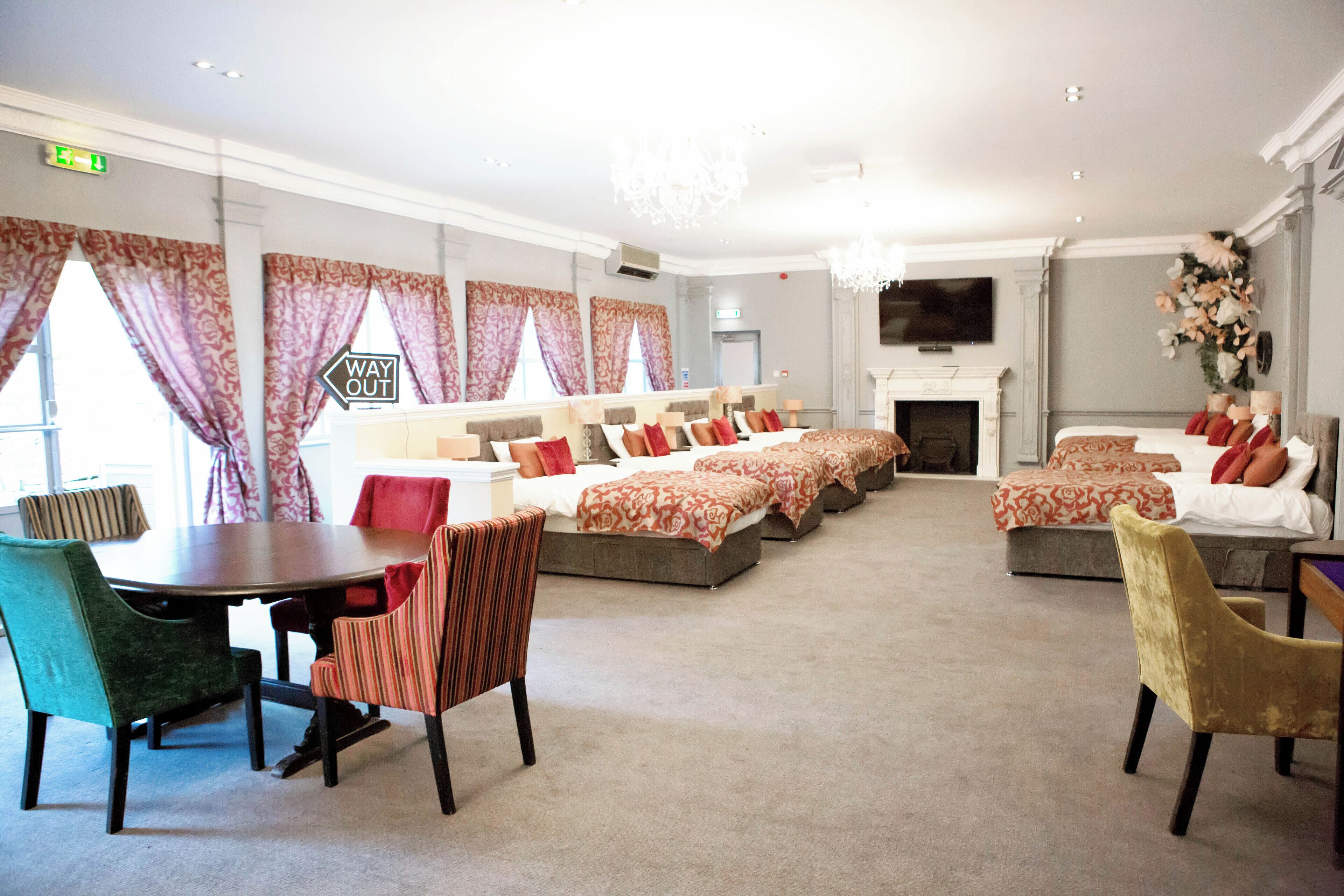 Habitación de hotel con comedor, múltiples camas con ropa de cama estampada, chimenea y televisor.