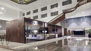 A spacious lobby with a modern staircase, a seating area with a sofa and chairs, and a decorative stained glass ceiling.