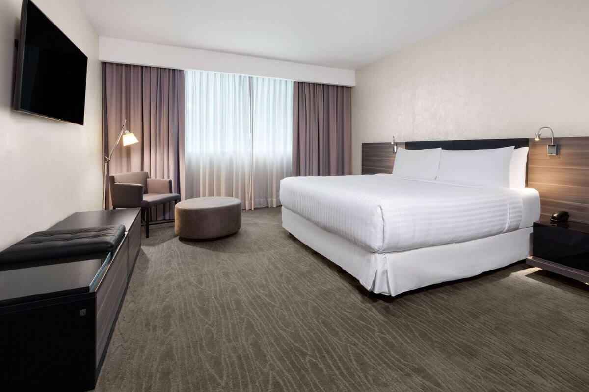A hotel room with a large bed, a desk, a chair, a TV, and a window with curtains.