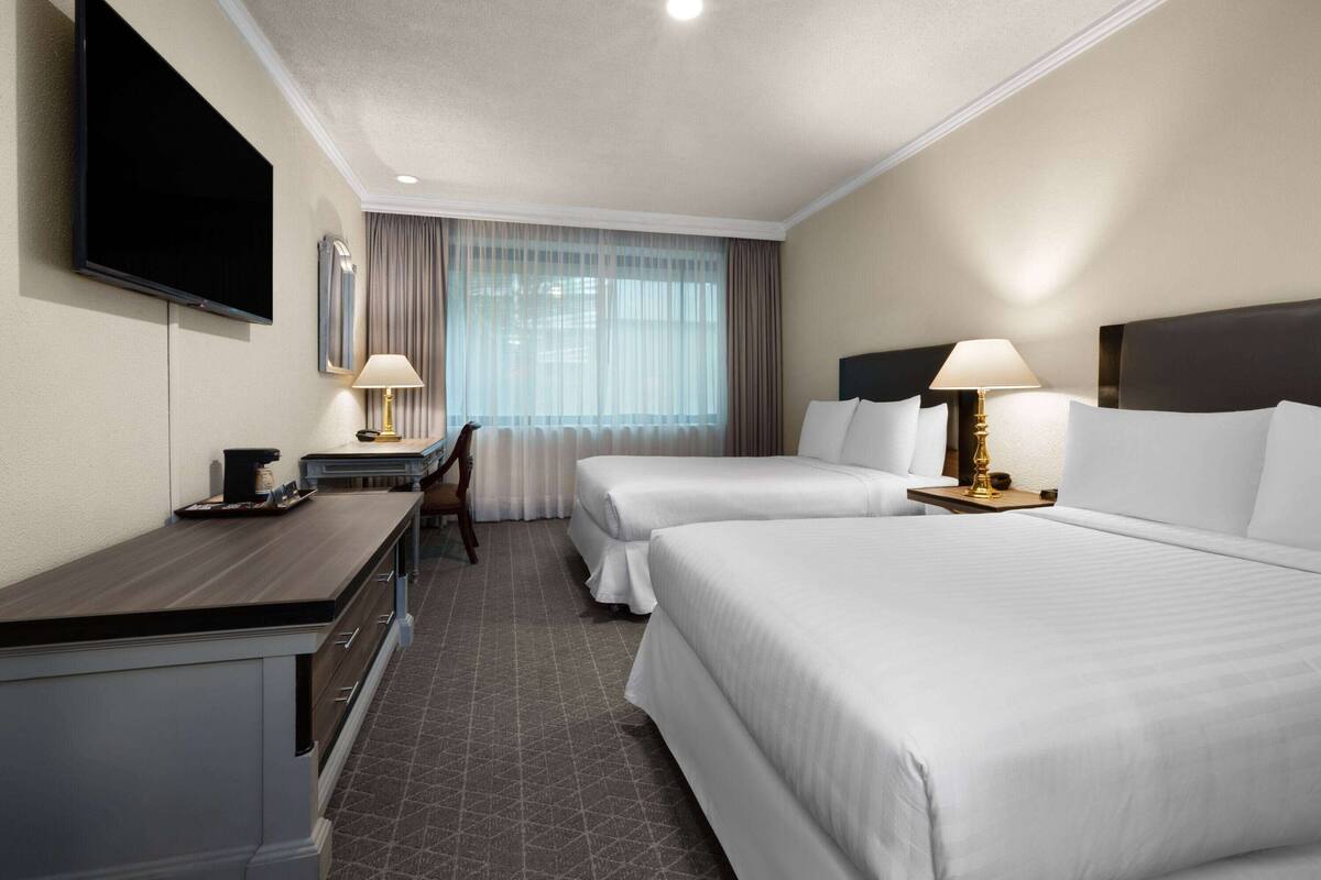 A hotel room with two beds, a desk with a lamp, a television, and a window with curtains.