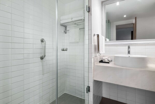 A modern bathroom with white tiled walls, a glass shower enclosure, a white sink, and a mirror above the sink.