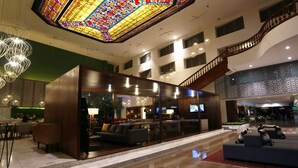 A spacious lobby with a staircase, seating area, and a large stained glass ceiling.
