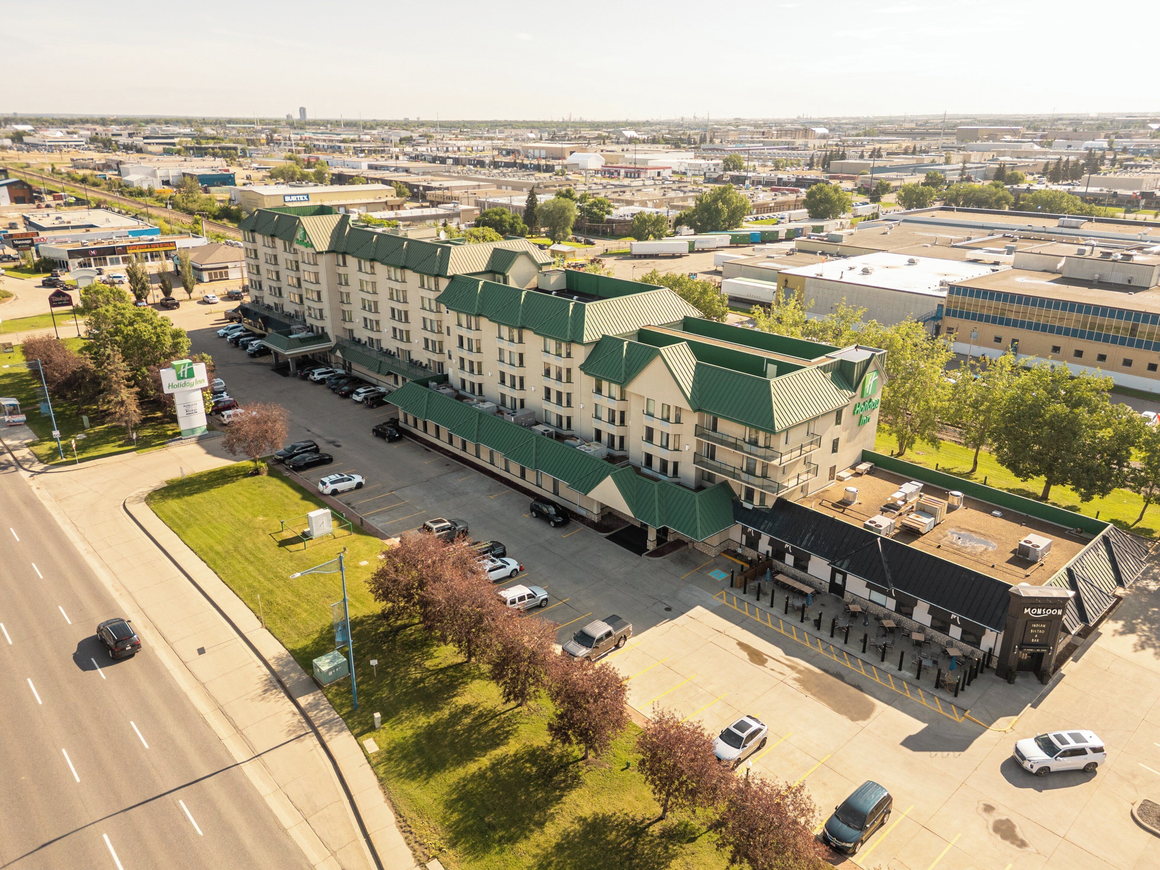 Un hotel Holiday Inn Express con techo verde, estacionamiento y edificios adyacentes.