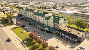 A Holiday Inn Express hotel with a green roof, parking lot, and adjacent buildings. - Holiday Inn Conference Center Edmonton South by IHG (Edmonton)