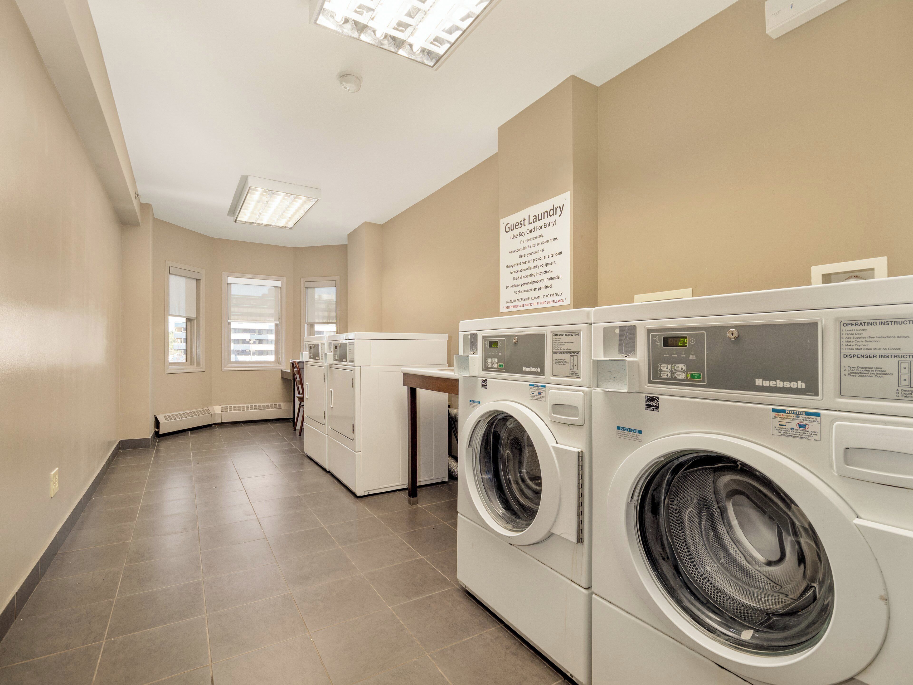 A laundry area with a sign indicating guest laundry use, a row of stacked washers and dryers, and a vented wall unit.