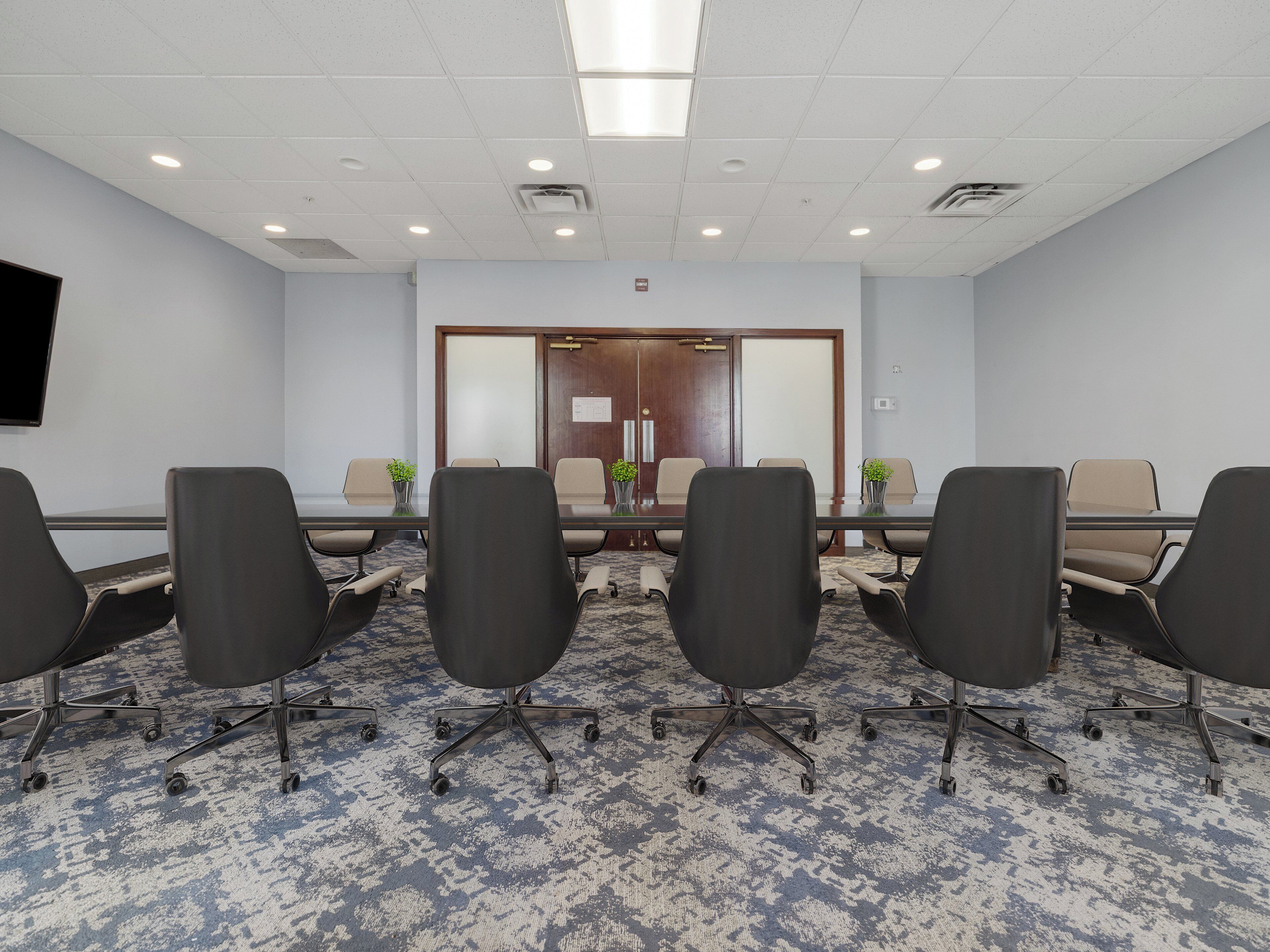 A conference room with a long table, six chairs, and a carpeted floor.