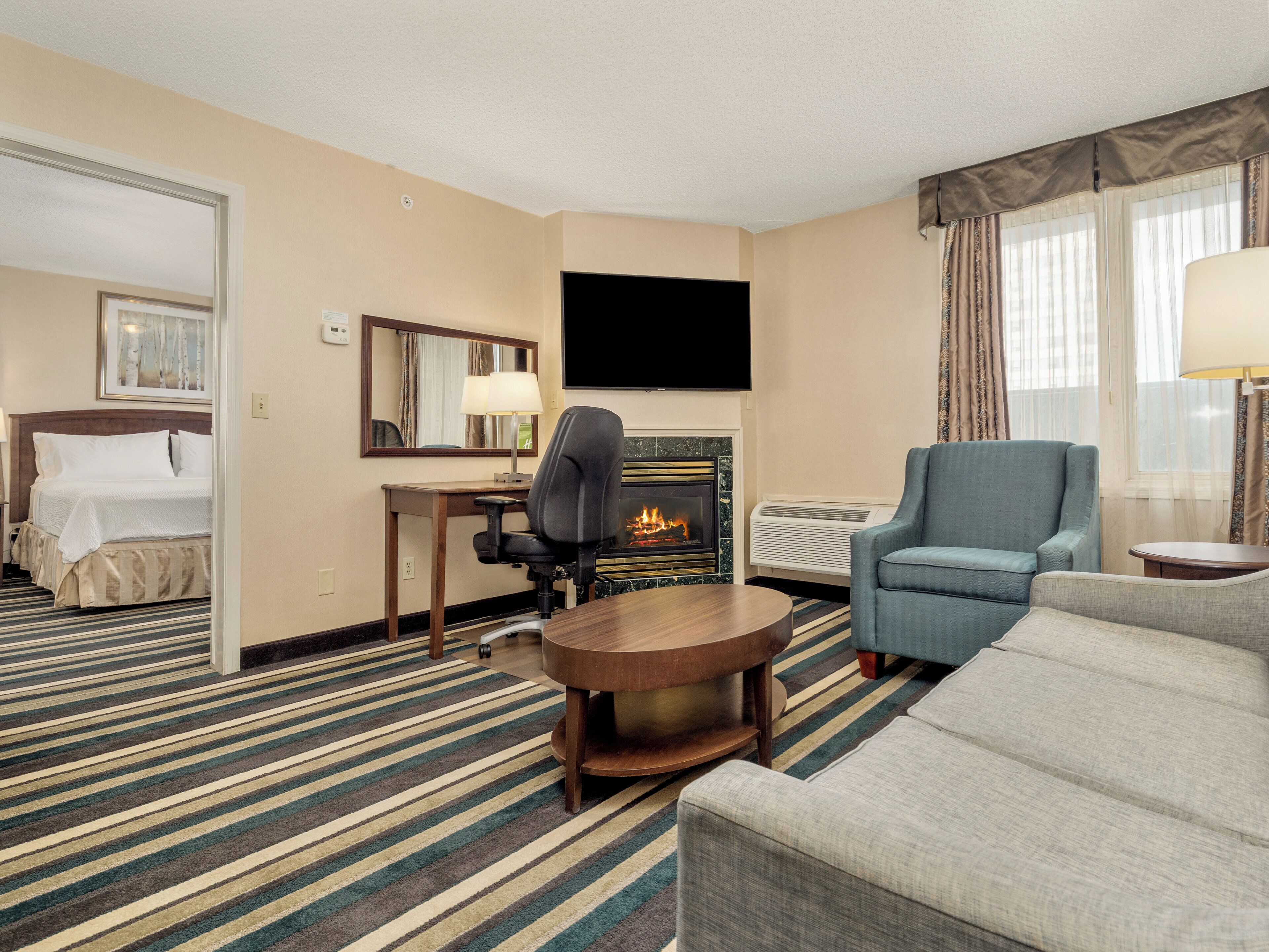 Une chambre d’hôtel comprenant un lit, un bureau avec une chaise, une télévision, une cheminée, un canapé et une fenêtre avec des rideaux.