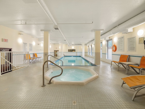 Un espace piscine comprenant un jacuzzi, des sièges et des panneaux d’indication des sorties.