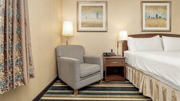 Una habitación de hotel con una cama, una silla, una mesita de noche, dos lámparas y dos cuadros en la pared.