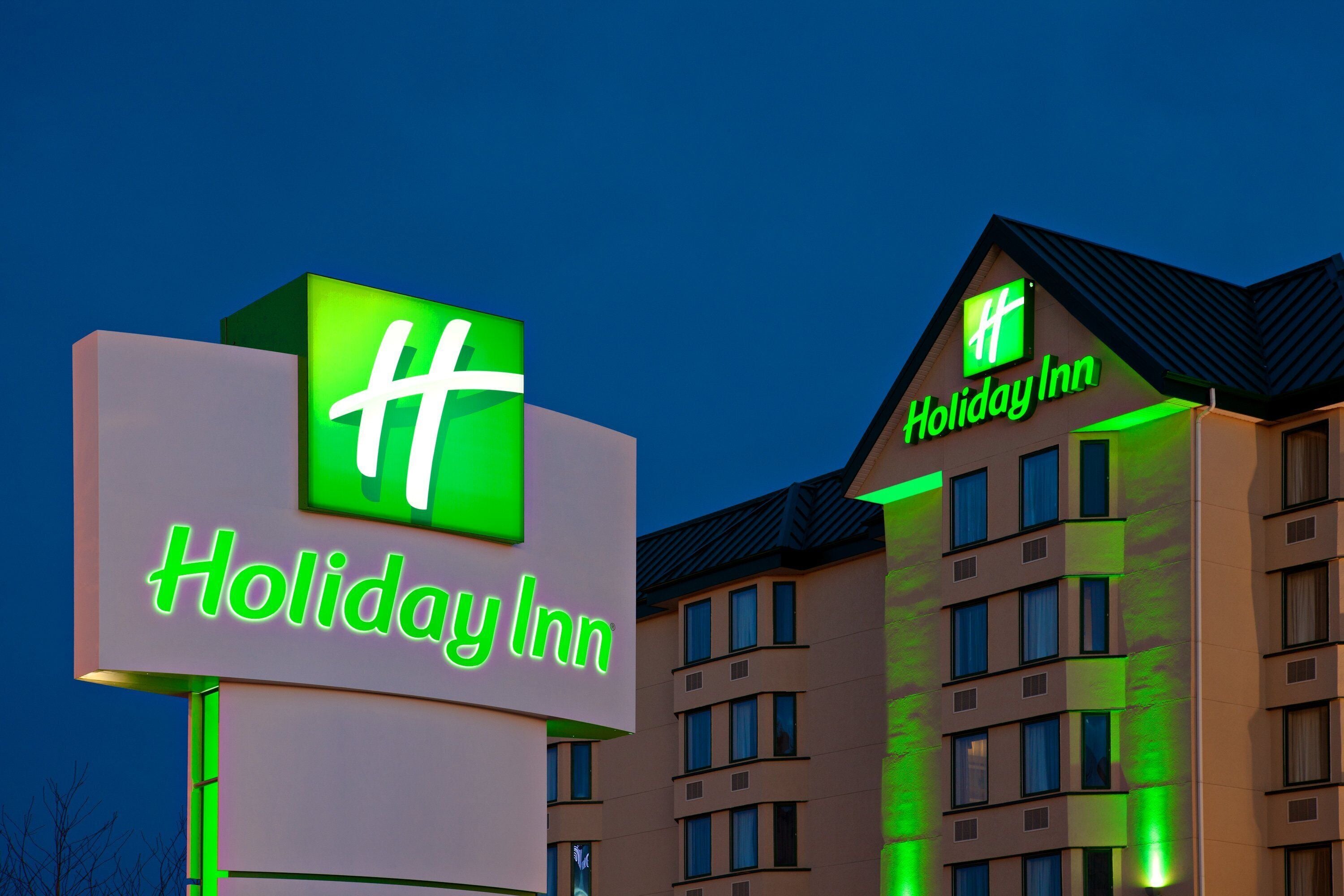 Une enseigne Holiday Inn avec un logo « H » bien visible et le nom « Holiday Inn » écrit en néon vert vif.