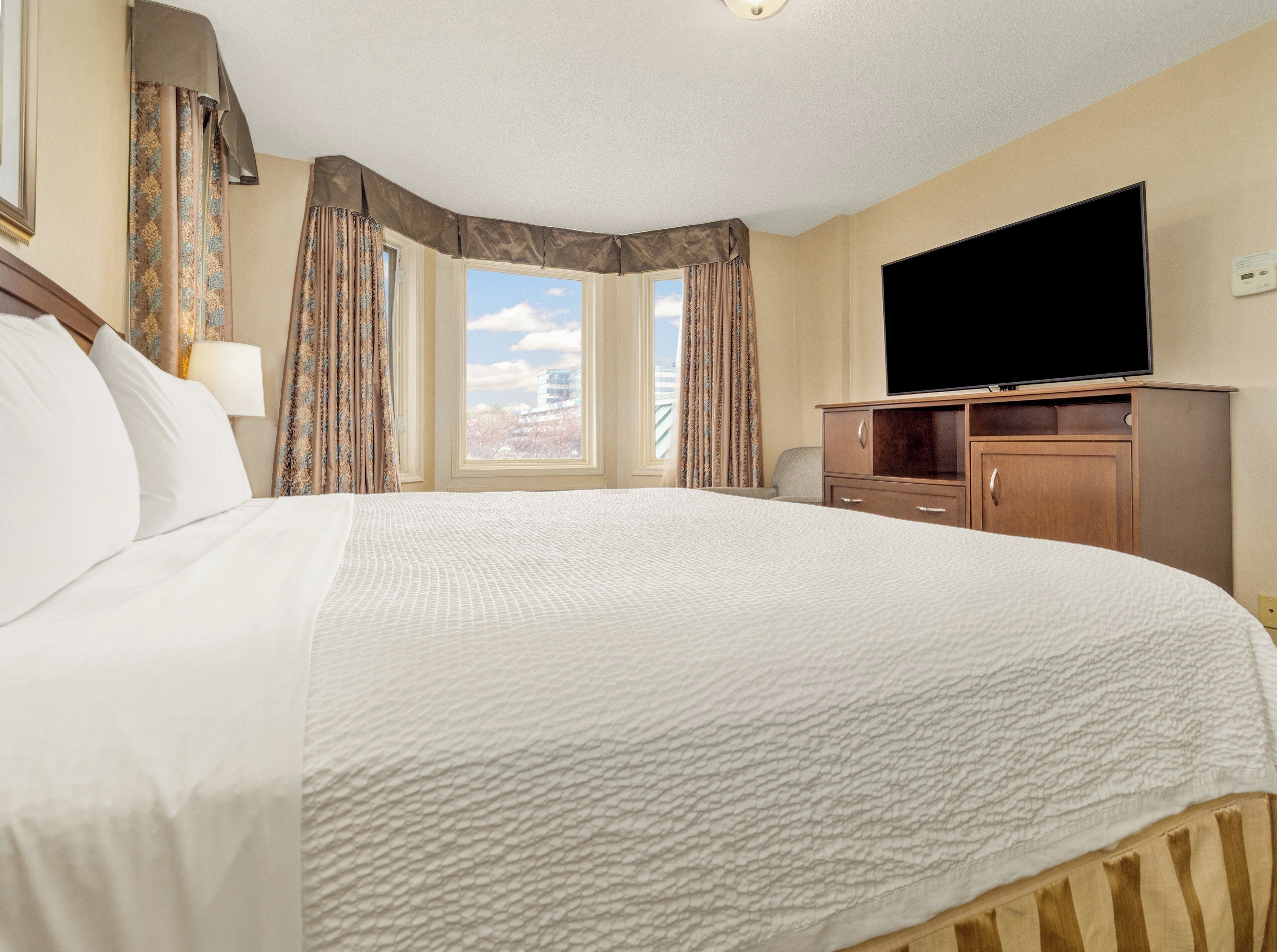 A hotel room with a large bed, a flat-screen TV, a wooden cabinet, and a window with curtains.