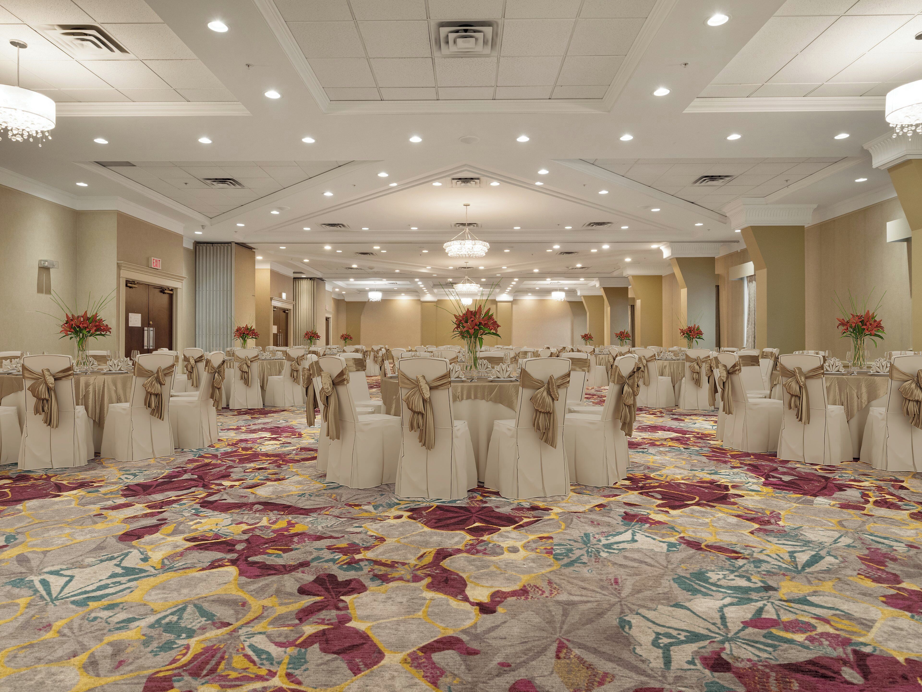 Une grande salle de banquet avec des tables rondes, des chaises de couleur beige et des centres de table ornés de compositions florales.