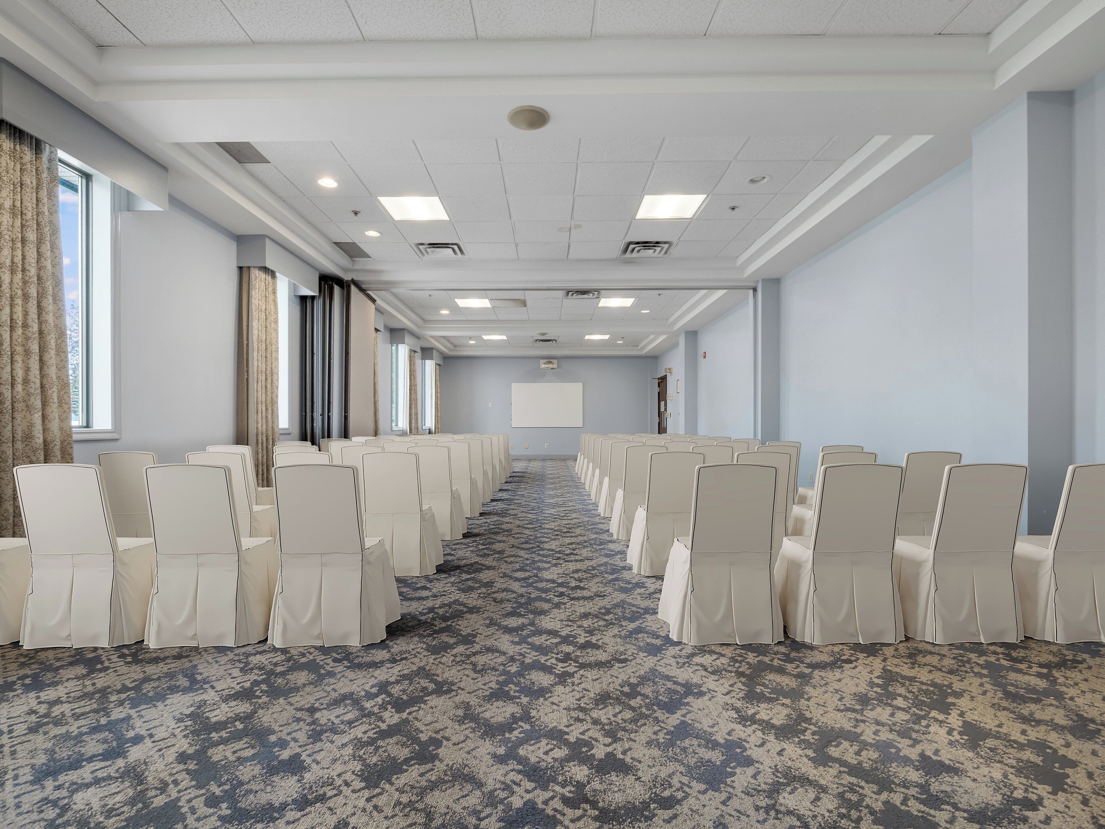 A conference room with rows of chairs, a projector screen, and large windows.
